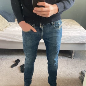 Blå skinny jeans från Diesel W28 - Säljer ett par blå skinny jeans från Diesel i storlek W28. Klassisk femficksmodell med snygga slitningar och röda Diesel-detaljer på fickan. Jeansen har låg midja och är tillverkade i stretchigt denim för en tight passform.
