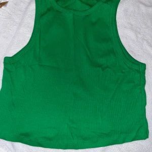 Croptop - Säljer en grön croppad linnetopp från H&M. Toppen är ärmlös med breda axelband och har en enkel, stilren design. Skön och stretchig känsla. Enbart testad