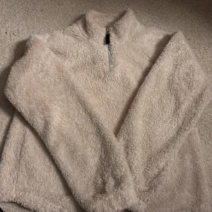 Beige fluffig fleece från Kappahl - Supermjuk och fluffig beige fleece-tröja från Kappahl med halv dragkedja framtill och hög krage. Perfekt för kyliga dagar och riktigt mysig att ha på sig. Långärmad och i en loose passform som ger en avslappnad vibe.