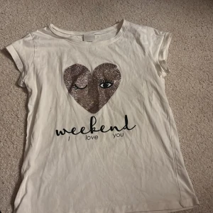 Vit t-shirt med glitterhjärta KappAhl - Vit t-shirt från Skön och mjuk bomull, perfekt att matcha till ett par Jeans