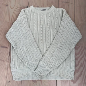 Beige kabelstickad tröja från GANT - Säljer en beige kabelstickad tröja från GANT i 100% bomull. Tröjan har klassiskt mönster med flätor, rund halsringning och ribbade muddar. Perfekt för lager-på-lager under höst och vinter. Supermjuk och stilren, passar till allt! Storlek M men passar även L