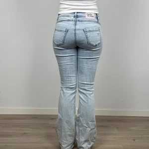 Ljusblå bootcut jeans Daily Denim - Snygga ljusblå jeans från Daily Denim med bootcut passform. Jeansen är mid rise med små rosa detaljer som gör dem unika. Perfekta för dig som gillar en avslappnad men trendig stil. Finns ingen storlekslapp men skulle säga att dem är 36/38