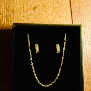 Guldplätering i sterling silver halsband och örhängen set - Säljer ett snyggt smyckeset med ett tvinnat guldigt halsband och matchande örhängen med glittrande stenar. Perfekt för dig som vill sticka ut med eleganta detaljer och lite extra bling.