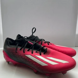 Adidas X Speedportal.1 SG - Snygga fotbollsskor från Adidas i en cool rosa och svart färg med vita ränder på sidan. Skorna har snörning och platt sula med dobbar för extra grepp på planen. Perfekta för dig som vill sticka ut och spela med stil. SKRIV FÖR FLER BILDER 