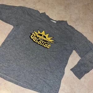 Grå långärmad tröja med biltryck - Säljer en grå långärmad tröja med coolt gult tryck av en retrobil och texten 'Gasoline' på bröstet. Tröjan har rund hals och är i mjukt material, perfekt för dig som gillar bilar och streetstyle.