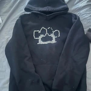 Svart hoodie med nitar och moln - Svart hoodie med huva och en unik design framtill gjord av silvriga nitar. Tröjan har en klassisk känguruficka och långa ärmar. Perfekt för dig som gillar streetstyle och vill sticka ut lite extra.