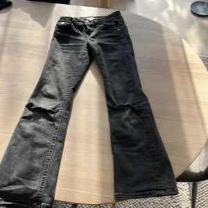 Svarta bootcut jeans från Gina Tricot - Svarta jeans från Gina Tricot i storlek 146 med bootcut-ben och slitningar vid knäna. Klassisk femficksmodell med knapp och dragkedja framtill. Jeansen har en cool, lite tvättad look och är tillverkade i bomullsmix för skön passform.