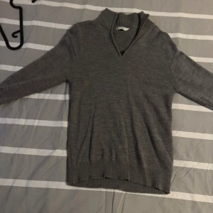 Grå merinoulltröja med half zip - Mysig grå tröja i 100% merinoull från C. Tröjan har ribbad krage och muddar samt en snygg half zip-dragkedja vid halsen. Perfekt för lager-på-lager och passar till både jeans och chinos. Passar 160