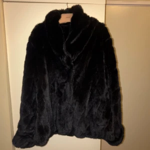 Svart pälsjacka med bred krage - Säljer en svart pälsjacka från NA-KD med bred krage och mjuk, fluffig känsla. Jackan har en klassisk, rak passform och är perfekt för dig som vill ha en cool och varm look under höst och vinter. Enkel att matcha med både jeans och boots.