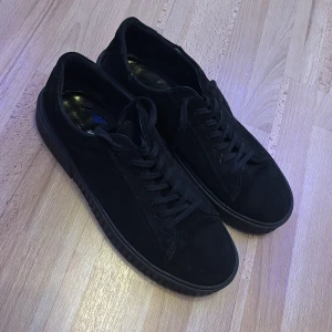Svarta mockaskor från Vagabond - Stilrena svarta sneakers från Vagabond i mocka med platt sula och snörning. Skorna har en klassisk och helsvart design som passar till det mesta. Perfekta för dig som gillar en clean och enkel look. Jag säljer dessa skor för jag kände att dem inte passade mig och var en storlek för stor. Ny pris för dessa skor när jag köpte dem var 1500 kr. Varan har små defekter men som inte påverkar helhets intrycket