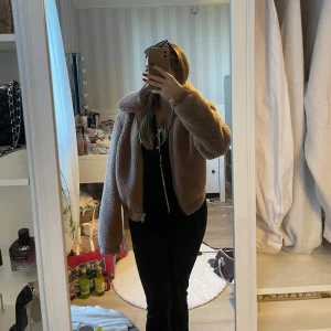Beige teddyjacka med dragkedja - Säljer en supermjuk och fluffig teddyjacka i beige med bred krage och dragkedja framtill. Jackan är croppad och har en oversized passform som ger en chill vibe. Perfekt för kyliga dagar när du vill vara både varm och snygg.