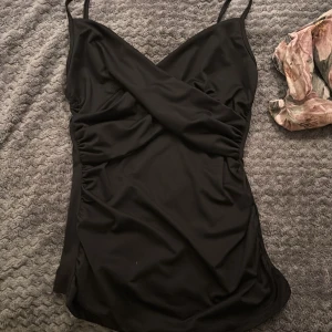 Svart omlott baddräkt med smala axelband - Ett snyggt svart linne med V ringat ich snygga detaljer 