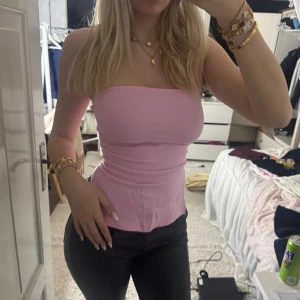 Ljusrosa bandeau tubtopp - Säljer en ljusrosa bandeau tubtopp med figurnära passform. Toppen är axelbandslös och har en lätt utsvängd nederkant med slits på sidorna. Perfekt för dig som gillar en clean och enkel look. Materialet känns mjukt och stretchigt.