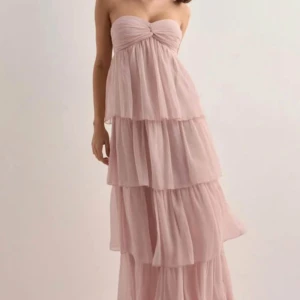 Ljusrosa volangklänning Nelly  - Superfin ljusrosa långklänning med flera lager volanger och bandeau-topp. Klänningen har en romantisk känsla med sitt luftiga chiffongtyg och kan bäras både axelbandslös eller med halterneck. Perfekt för dig som vill ha en flowy och feminin look. Helt oanvänd, provat en gång och kom fram till att det inte är min färg. Säljer den här pga av att jag missade retur tiden hos Nelly och kunde därför inte skicka tillbaks den. 700kr nypris