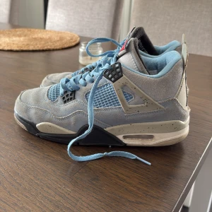 Nike Air Jordan 4 University Blue - Nike Air Jordan 4 University Blue med ljusblå mocka, meshpaneler och svarta detaljer. Snygg specklad mellansula, klassisk Jumpman-logga under sulan och blå skosnören. Perfekta sneakers för dig som vill sticka ut med en ikonisk modell.
