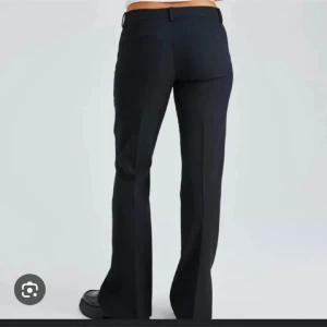 Svarta kostymbyxor med slits - Snygga svarta kostymbyxor med slits och låg midja. Byxorna har klassiska fickor fram och hällor för bälte. Perfekta för en clean och stilren look, passar till sneakers eller boots. Materialet är slätt och ger en dressad känsla.