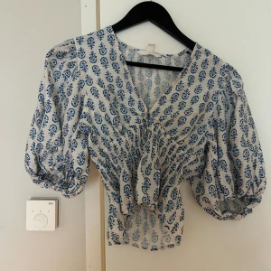 Vit och blå blommig blus med puffärm - Säljer den virala sommar blusen från hm med smockad tyg runt midjan och en v-ringning.                                                                     