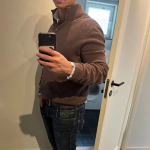 Brun half zip tröja Morris Stockholm passar M - Säljer en brun långärmad tröja från Morris Stockholm med half zip och hög krage. Tröjan är stickad i bomull och har en diskret broderad logga på bröstet. Perfekt för lager-på-lager och snygg till jeans.