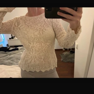Vit stickad blus med spetsdetaljer - Säljer en vit stickad blus med långärmade ärmar och vackra spetsdetaljer. Blusen har ett genombrutet mönster och vågig kant vid ärmslut och nederkant. Perfekt för dig som gillar romantisk och bohemisk stil.