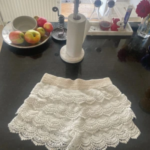 Vita shorts med volang - Säljer ett par vita shorts med elastisk midja och flera lager volangdetaljer. De har en snygg scallop-kant och är perfekta för sommarens alla häng. Passformen är normal och materialet känns som bomull.