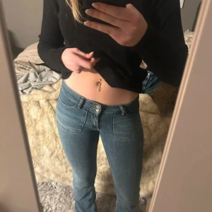 Blå bootcut jeans med stora fickor - Snygga ljusblå jeans med bootcut och stora fickor bak med knappar. Hög midja och klassisk jeanslook med synliga sömmar. Perfekta för dig som gillar retrovibbar och vill ha ett par jeans som sticker ut lite extra.