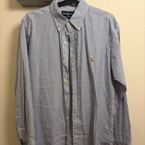 Randig skjorta från Ralph Lauren - Klassisk blåvit randig skjorta från Ralph Lauren med broderad logga på bröstet. Skjortan har knappar hela vägen, button-down krage och är tillverkad i 100% bomull. Perfekt för en clean och stilren look. Vintage. Inköpt i Tokyo