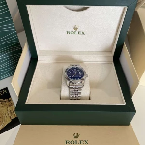 Datejust blå urtavla stål - Säljer en stilren Datejust med blå urtavla och klassisk räfflad bezel. Klockan har ett snyggt jubilee-armband i rostfritt stål och levereras komplett med originalbox, certifikat och tillbehör. Perfekt för dig som gillar exklusiva accessoarer.