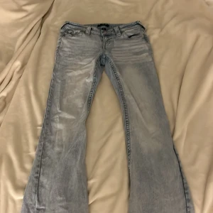 True Religion Joey Low Rise Flare Jeans - Snygga ljusblå jeans från True Religion, modell Joey Low Rise Flare. De har låg midja och utsvängda ben, klassiska detaljer med stora bakfickor och silverfärgade knappar. Perfekta för dig som gillar en retro och avslappnad stil.dom har tyvärr inte blivit använda mer en 1 gång pg av att midjan e förstor dom är uppsydda så att dom passar mig som är 150cm dom har tappat en bak knapp som ni får med och kan försöka lösa💕💕💕