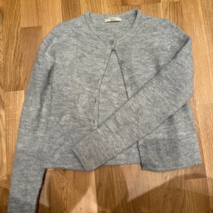 Grå kofta från Gina Tricot XS - Mysig grå kofta från Gina Tricot i storlek XS. Koftan har rund halsringning, långa ärmar och knäppning framtill med matchande knappar. Tillverkad i ett mjukt och stickat material som passar perfekt till lager-på-lager-stil.