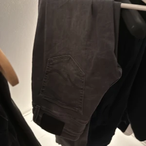 Replay grå jeans slim fit 30/32 - Snygga grå jeans från Replay i modellen slim fit. Jeansen har klassisk femficksdesign, svarta detaljer och en diskret tvättad look. Passar dig som gillar en smalare siluett och vill ha ett par stilrena jeans med modern känsla.