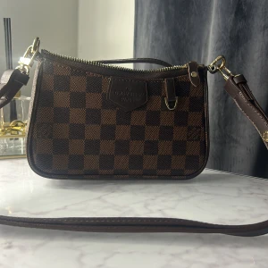 axelväska brun - Snygg axelväska i klassiskt brunt rutigt mönster. Väskan har guldfärgade metalldetaljer, dragkedja och justerbar axelrem. Perfekt storlek för det viktigaste och en ikonisk accessoar till din outfit. Gått sönder lite vid handtaget 