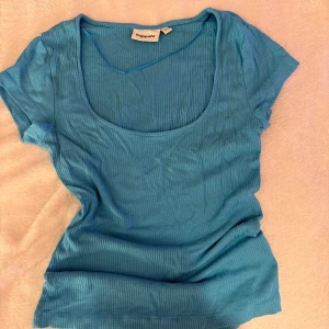 Blå ribbad topp från Kappahl - Säljer en blå ribbad topp från Kappahl i storlek S. Toppen har korta ärmar, rundad djup urringning och är tillverkad i ett mjukt, stretchigt material som sitter snyggt på kroppen. Perfekt för dig som gillar en enkel men stilren look.
