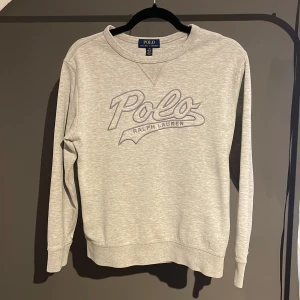 Grå sweatshirt från Polo Ralph Lauren - Snygg grå sweatshirt från Polo Ralph Lauren med stort broderat logotryck på bröstet. Tröjan har rund hals, långa ärmar och är gjord i mjuk bomullsmix. 
