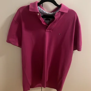 Rosa pikétröja Tommy Hilfiger M - Snygg rosa pikétröja från Tommy Hilfiger i storlek M. Klassisk krage, korta ärmar och liten logga broderad på bröstet. Tillverkad i mjuk bomull som känns skön mot huden. Perfekt för dig som gillar stilrena och färgstarka plagg.
