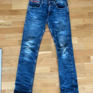 Blå jeans från Replay - Säljer ett par blå slim fit jeans från Replay med snygga slitningar och broderad Replay-logga på bakfickan. Jeansen har klassisk femficksdesign, normalhög midja och är tillverkade i jeansmaterial. Perfekta för dig som gillar en smal passform och coola detaljer. Notera hålet i vänster knät.