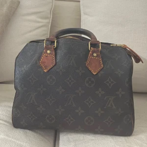 Louis Vuitton speedy  handväska 25 - Klassisk Louis Vuitton Speedy handväska i mörkbrunt skinn med ikoniskt monogrammönster och detaljer i ljusbrunt läder. Det är en storlek 25 . Den är köpt här på plick. Jag har behövt byta handtag på en sida som ni ser men inget som någon eller jag tänker på. Den bruna skinnbitten på dragkedjan är borta . Därav pris men annars en väldigt fin och snygg väska . Hör av er till mig ifall ni undrar något specifikt 🥰ingår en orangiserings väska  dessutom ifall man önskar det 