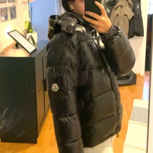Svart Moncler pufferjacka M - Säljer en svart pufferjacka från Moncler i storlek M. Jackan har glansig yta, huva och dragkedja framtill. Klassisk Moncler-logga på ärmen. Säljer den då jackan har blivit för stor för mig