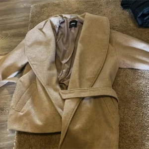 Beige omlott kappa från ONLY - Säljer en beige kappa från ONLY i omlottmodell med bälte i midjan och bred krage. Jackan har en stilren look och är tillverkad i ett mjukt material som känns lyxigt. Perfekt för dig som gillar minimalistisk och clean stil.