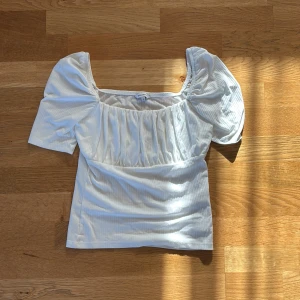 Vit blus med puffärm - Säljer en vit blus från Gina Tricot med puffiga korta ärmar och fyrkantig ringning. Blusen har lätt rynkade detaljer framtill och är gjord i mjuk bomull. Perfekt för dig som gillar romantisk och trendig stil. Använd fåtalet gånger och köpt för 350. 