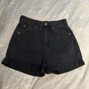 Svarta jeansshorts från H&M Divided - Säljer ett par svarta jeansshorts från H&M Divided i storlek 34. De är högmidjade med klassisk femficksdesign, uppvikta benslut och stängs med knapp och dragkedja.