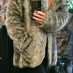 Grå pälsjacka från KappAhl - Säljer en fluffig och snygg grå pälsjacka från KappAhl. Jackan har lång ärm, bred krage och silkeslen grå insida. Perfekt för dig som vill sticka ut och hålla dig varm med stil. Jackan har en loose passform , med silvrigt foder och två fickor.  Hel, förutom att det bara är mittenhyskan som finns kvar , lite lös. 