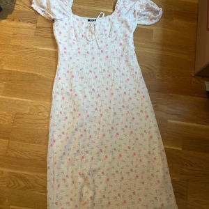 Blommig sommarklänning från Gina Tricot - Supersöt ljus klänning med rosa blommor från Gina Tricot. Klänningen har kort puffärm, knytning vid bysten och är gjord i ett skönt bomullstyg. Perfekt för varma dagar och har en romantisk vibe med sitt blommiga mönster.