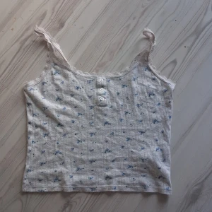Supergulligt linne🦋🪻💙🩵 - Supersöt linnetopp från new yorker i storlek S. Toppen är vit med små blå blommor, spetskant runt halsringningen och axelbanden samt dekorativa knappar framtill. Tillverkad i mjuk bomull och har en romantisk vibe med rosett på etiketten.