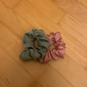 Två scrunchies i satin, grön & rosa - Säljer två snygga scrunchies i satin, en i dämpad grön och en i mjuk rosa. Perfekta för att piffa upp håret och ge en lyxig känsla till din look. Båda är stora och fluffiga, vilket gör dem till ett statement i håret.