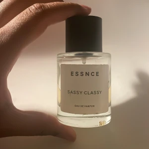 ESSNCE Sassy Classy Eau de Parfum - Parfymflaska från ESSNCE med doften Sassy Classy. Flaskan är cylindrisk i genomskinligt glas med svart lock och vit etikett. Innehållet är ljusgult och flaskan har en stilren, minimalistisk design. Perfekt för dig som gillar moderna och fräscha dofter. OBS! Hälften kvar och går inte ner i pris.