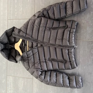 Svart colmarjacka - Snygg svart pufferjacka från Colmar med luva. Skick: 10/10. Enbart använd ungefär 7 gånger, och har ings tecken på användning. Hanterar kyla utmärkt, och håller samtidigt en bra stil.