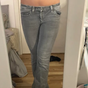 Grå bootcut jeans - Säljer ett par grå jeans med bootcut passform. Jeansen har klassiska fickor med dekorativa sömmar och silverfärgade knappar bak. Perfekta för dig som gillar en avslappnad men trendig look. Säljer dem då dem är för små. Dem är sprättade nertill men det är inget som märks. Pris kan diskuteras💞