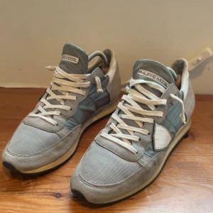  Philippe Model sneakers  - Snygga sneakers från Philippe Model i grå toner med detaljer i mocka och textil. Skorna har snörning, rund tå och platt sula. Stilren design med logotyp på sidan och bekväm innersula i skinn. Perfekta för dig som gillar en clean och urban look. Strl 41