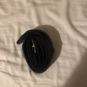 Mörkblå flätat bälte med silverfärgat spänne - Snyggt mörkblått bälte med flätad design och silverfärgat spänne. Bältet har en stilren look och är gjort i ett textilmaterial som ger en cool och avslappnad känsla. Perfekt för att lyfta vilken outfit som helst.