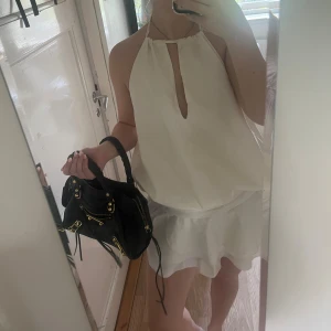 Vit omlottklänning från Aloruh - Supersöt vit kortklänning från shein med omlottvolanger i kjolen och halterneck med snygg öppning framtill. Klänningen har en luftig passform och är tillverkad i ett lätt, mjukt material som ger en skön känsla. Perfekt för sommarens alla tillfällen!